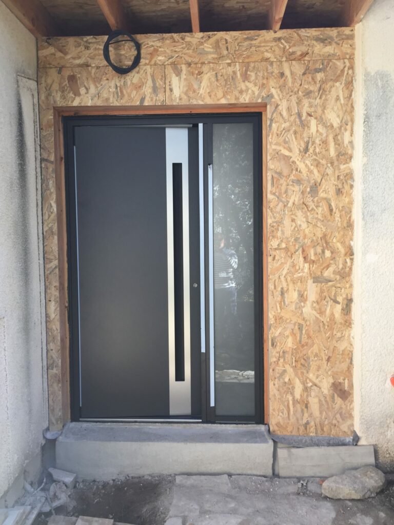 Grande porte d'entree moderne grise avec barre de tirage argent ouvrant tierce vitre